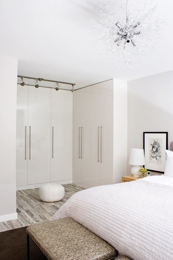 a neutral and chic bedroom with a gorgeous chandelier and a closet organized here, with sleek doors for a decluttered look
