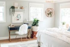 a pretty boho bedroom with a navy desk and a faux fur chair, a floating shelf and potted plants, neutral bedding and a printed rug
