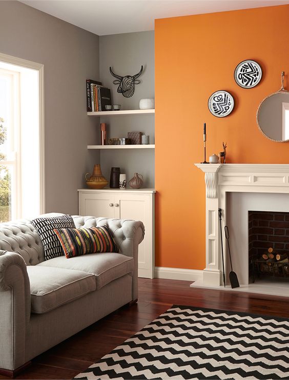 a pretty monochromatic mid-century modern living room done in grey, black and white and cheered up with a bold orange accent wall