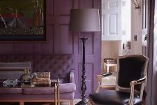 a refined living room with a purple accent wall and a matching sofa, a refined table with gold legs, a black leather chair and a grey floor lamp