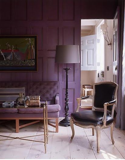 a refined living room with a purple accent wall and a matching sofa, a refined table with gold legs, a black leather chair and a grey floor lamp