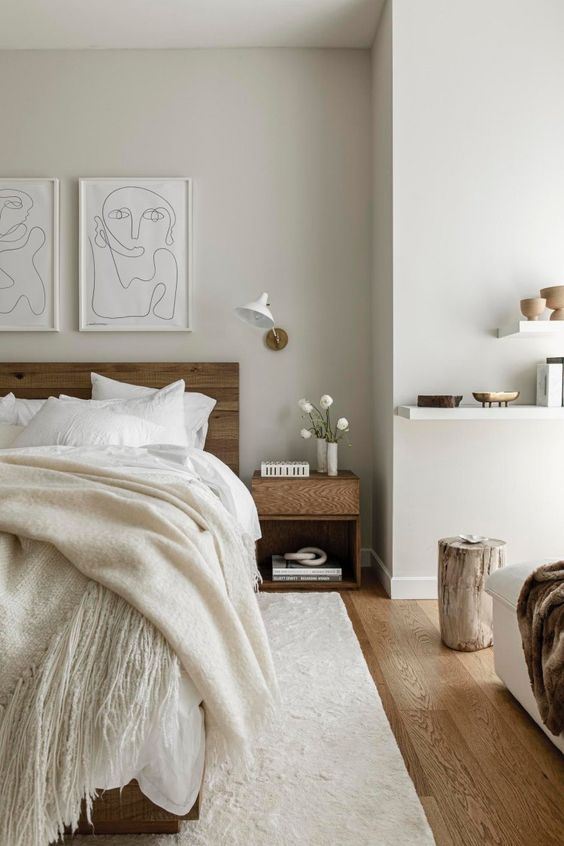 a refined minimalist bedroom with stained furniture, a floating shelf, tree stumps, sconces, a grid gallery wall and neutral textiles