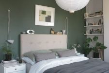 a relaxing modern bedroom with a green accent wall, open shelves, an upholstered bed with neutral bedding, white nightstands and a pendant lamp