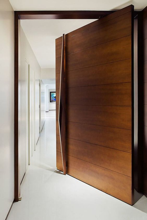 A rich stained wood clad pivot door with a large and sculptural handle that adds a refined and chic touch to the space