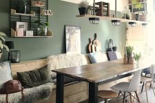 a rustic dining room with a green accent wall, a wooden table and mismatching chairs, a wooden built-in bench with lots of pillows