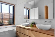 a simple contemporary bathroom with a window, a tub, a concrete tile floor, a double light-stained vanity and a mirror storage unit
