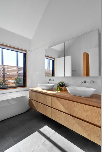 A simple contemporary bathroom with a window, a tub, a concrete tile floor, a double light stained vanity and a mirror storage unit