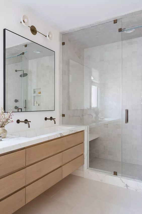 a sleek contemporary bathroom with a shower space clad with marble, a floating vanity with a marble countertop, a mirror and brass fixtures