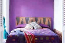 a small and colorful boho bedroom with a purple accent wall, a bed with bright bedding, a small stool and a Moroccan pendant lamp