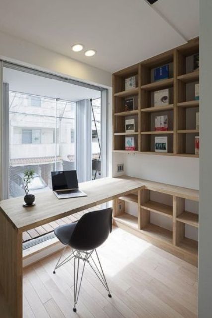 A small contemporary home office with open stained storage units, a built in desk, a black chair and a glazed wall for a view