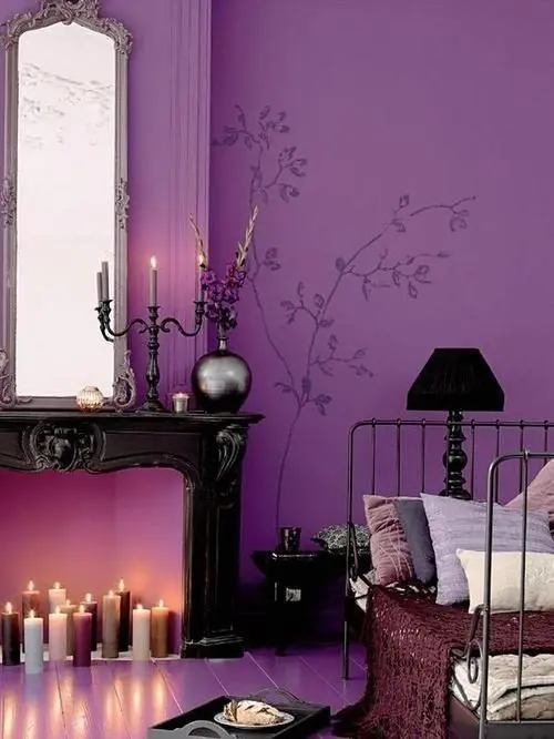 A sophisticated bedroom with a purple accent wall, a non working fireplace with candles, a vintage metal bed with pillows and elegant decor