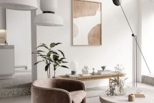 a sophisticated contemporary living room with a curved dusty pink chair, a round coffee table, a wooden bench, potted greenery, astatement artwork and lots of lamps