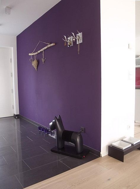 a statement entryway with a deep purple accent wall, candleholders right on the floor, a quirky floor lamp and some decor on the wall