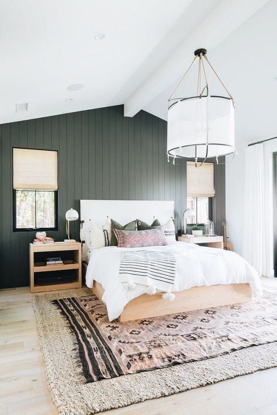 a stylish bedroom with a graphite grey planked accent wall, a neutral bed and printed bedding, matching nightstands and a pendant lamp