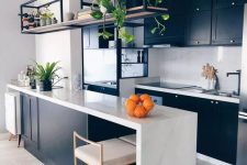 a stylish contemporary kitchen with black cabinetry, alarge kitchen island with a waterfall countertop, a black metal shelf and black fixtures