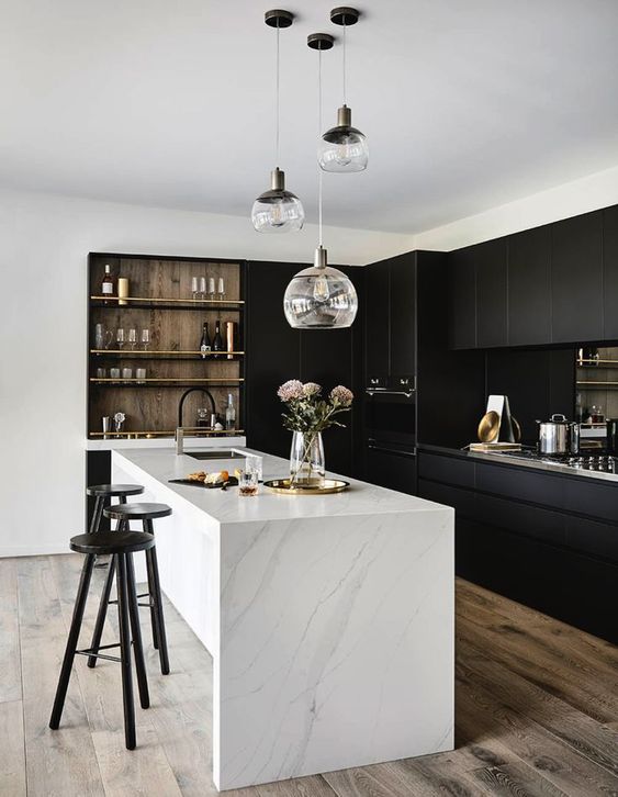 A stylish contrasting kitchen with sleek black cabinets, a white stone kitchen island, built in shelves and a cluster of pendant lamps