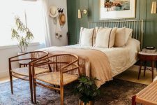 a stylish modern boho bedroom with a green paneled accent wall, a gilded bed, woven chairs and a bench, with printed bedding