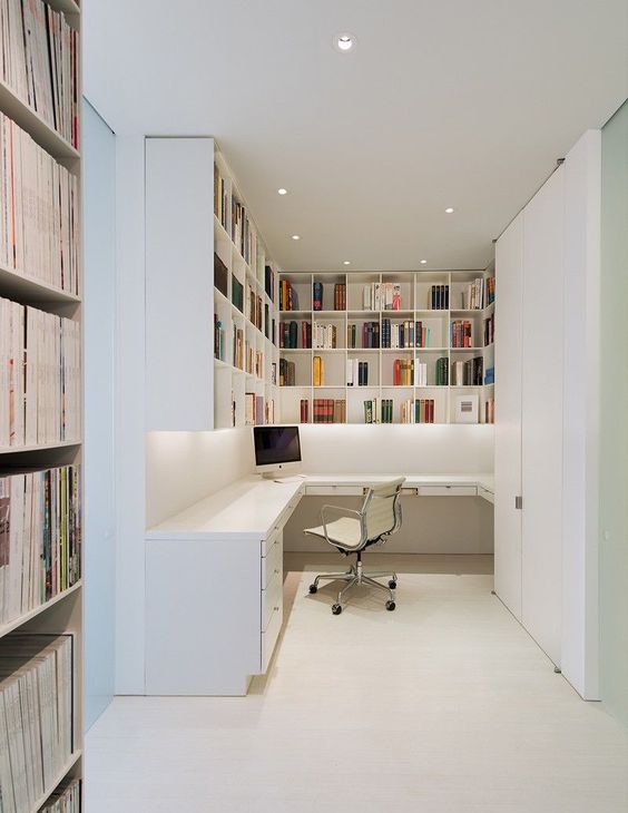 A very simple contemporary home office nook with lots of shelves for storage, a corner desk, a white chair and built in lights
