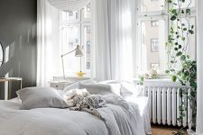 an airy Scandinavian bedroom with a black accent wall, a bed with neutral bedding, a climbing plant and neutral textiles