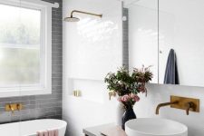 an airy contemporary bathroom with a grey subway tile accent wall, blue and white tiles on the floor, a floating vanity, brass fixtures and a window