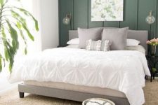 an organic bedorom with a green paneled accent wlal, a grey upholstered bed, neutral bedding, layered rugs and a botanical artwork and a potted plant