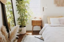 02 a beautiful and light-filled bedroom with an upholstered bed, a floor mirror, macrame hanging, pampas grass and a potted plant