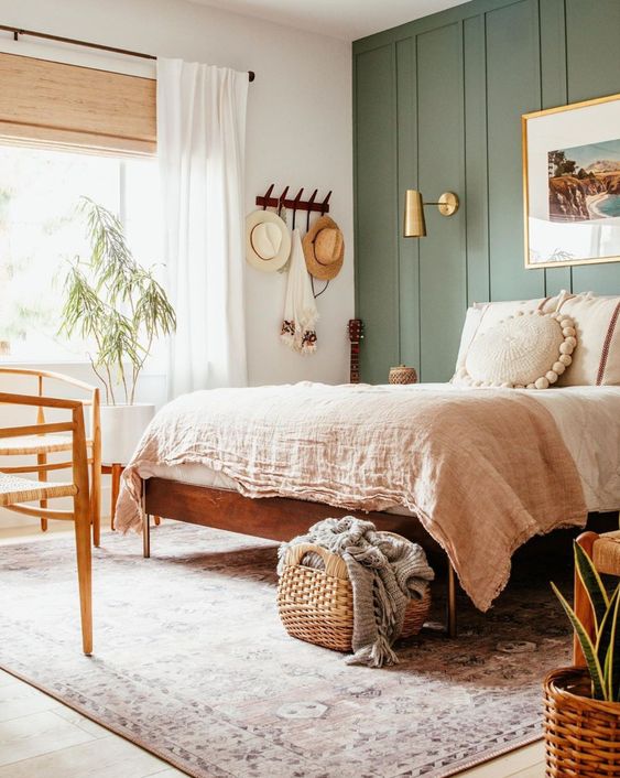 a cozy boho bedroom with a green accent wall, stained furniture, a shelf with hats, neutral bedding and a potted plant is welcoming and cool