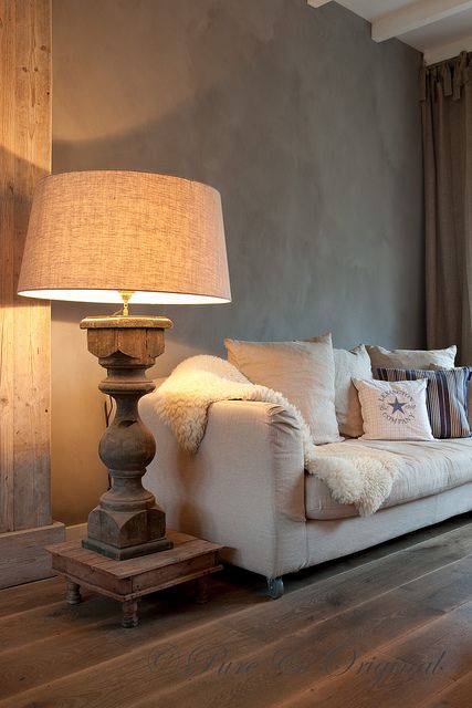 a refined taupe living room with rich stained floors, a creamy sofa, a wooden stand with an oversized lamp on a wooden carved stand
