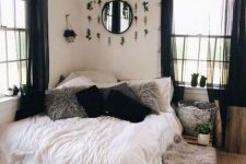 09 a lovely boho bedroom with white walls, a pallet bed, neutral bedding, grey and black pillows, a mirror with faux greenery and black curtains