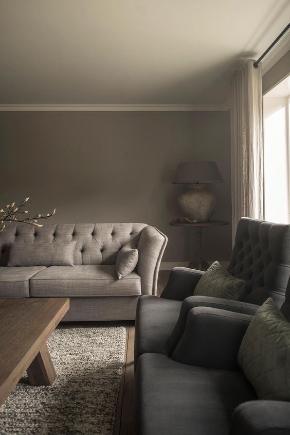 a taupe living room with a greige sofa, grey chairs, a printed rug, a wooden coffee table and a large table lamp