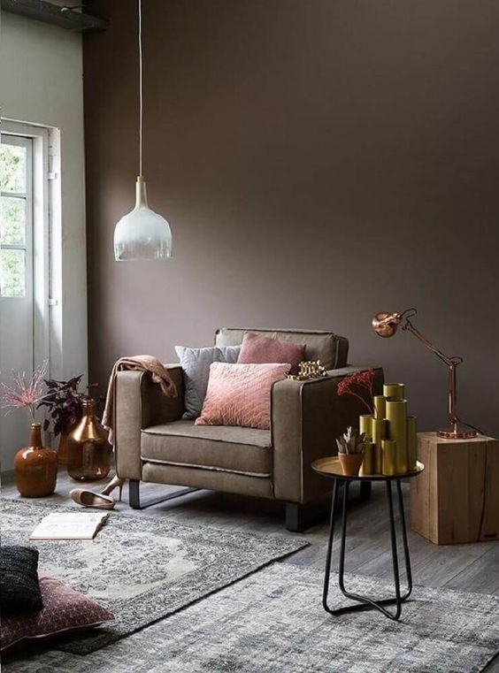 a taupe living room with a taupe chair, a tree stump and a metal side table, lots of vases, potted plants and layered rugs