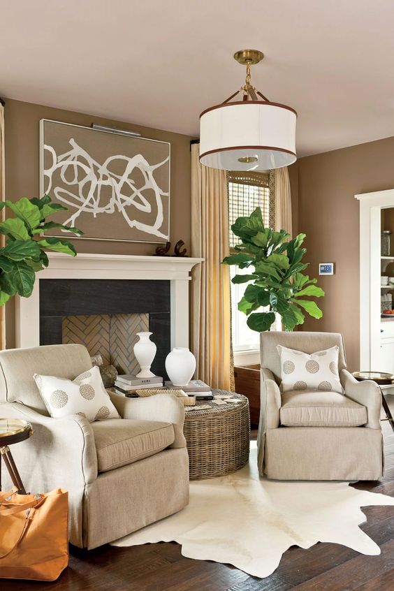 A welcoming taupe living room with a vintage styled fireplace, tan chairs, a woven coffee table, statement potted plants and polka dot pillows