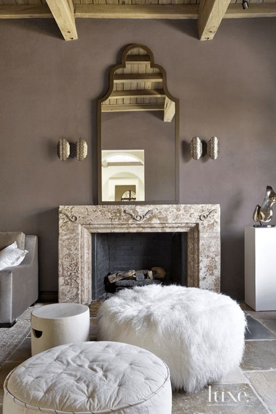An exquisite taupe living room with a non working fireplace, a refined mirror, metallic sconces, white ottomans and poufs and taupe furniture