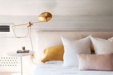 19 a dreamy and serene bedroom with white planked walls, a neutral upholstered bed, white and yellow bedding and a gold sconce is chic