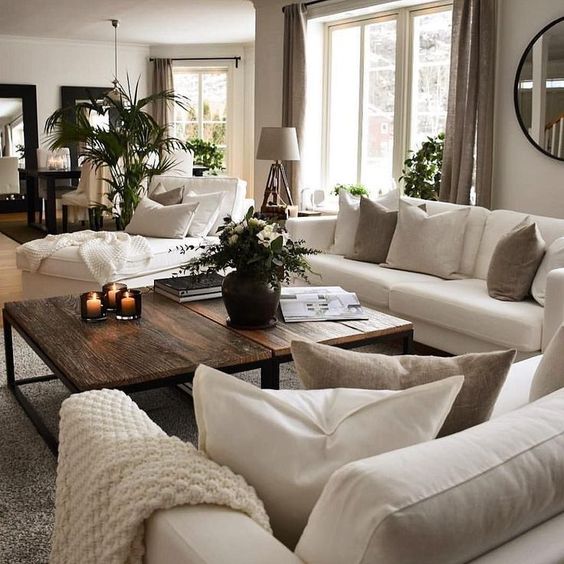 A grey living room with creamy sofas and a lounger, taupe and creamy pillows, taupe curtains, a duo of rich stained coffee tables