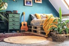 25 an attic bedroom with a pallet bed, yellow and grey bedding, a navy accent wall, a green dresser, a plywood map on the wall, layered rugs and potted plants