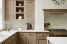 a beautiful taupe vintage kitchen with shaker cabinets, white countertops and a backsplash, a cooker with a hood, a catchy clock and vintage knobs