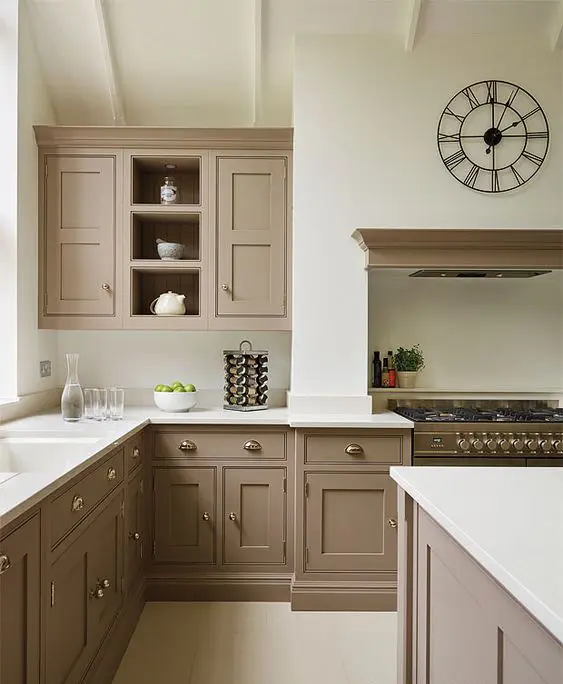 A beautiful taupe vintage kitchen with shaker cabinets, white countertops and a backsplash, a cooker with a hood, a catchy clock and vintage knobs