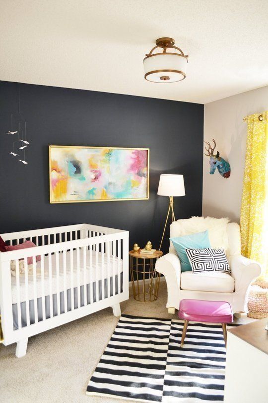 a bold nursery with a black accent wall, a striped rug and printed pillows, a pink stool and a bright artwork plus faux taxidermy is amazing