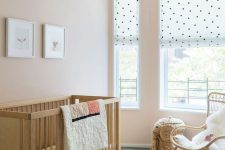 a catchy contemporary nursery with blush walls, stained wood and rattan furniture, a pendant lamp, layered rugs and polka dot shades