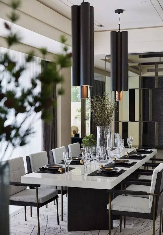 a chic contemporary dining space with a white table with black legs, black chairs with white upholstery, black pendant lamps and greenery