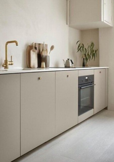 a chic contemporary kitchen with only lower cabinets in taupe, with bolg knobs and fixtures, with white stone countertops and a single white upper cabinet