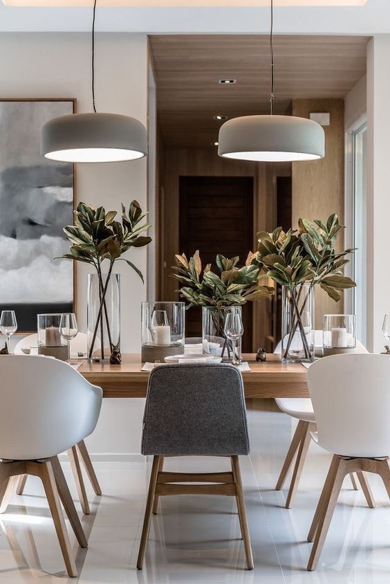 a chic neutral contemporary dining room with a light-stained table, white and grey chairs, pendant lamps, candles and foliage