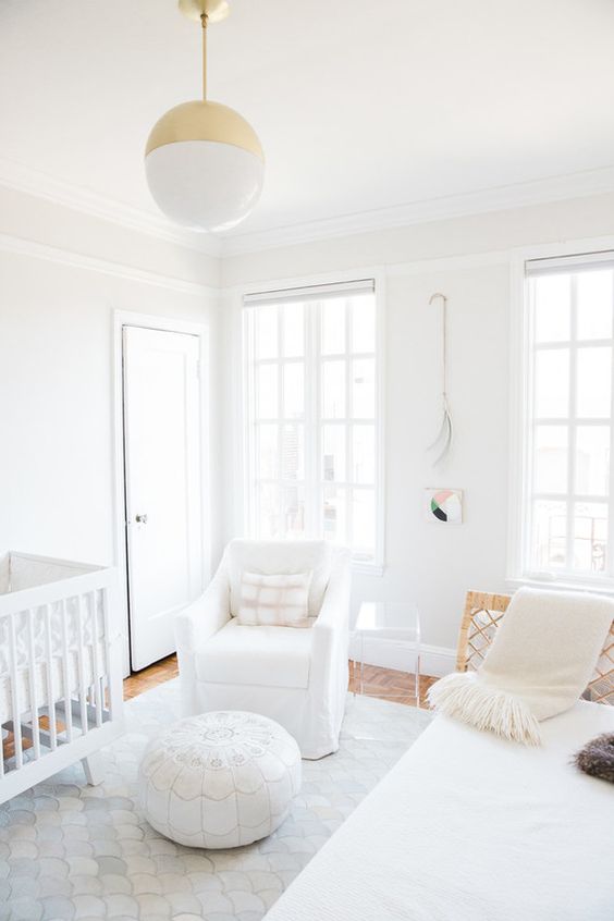 a clean white contemporary nursery with cool furniture, a Moroccan ottoman, a gold and white pendant lamp and neutral textiles