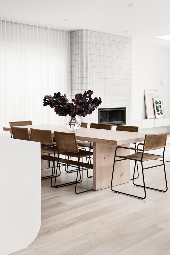 A contemporary dining room with a sleek light stained table, leather chairs, a fireplace clad with white tiles
