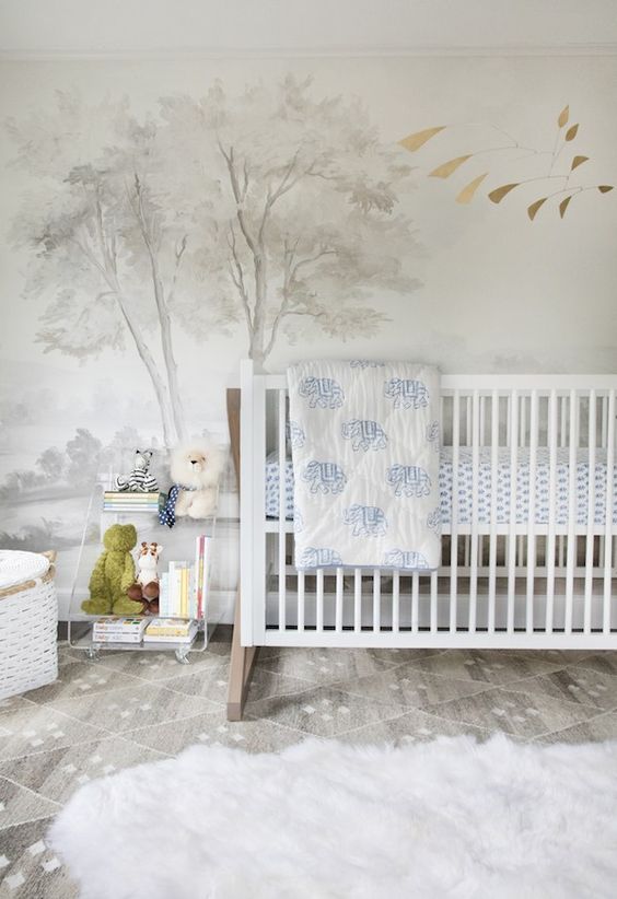 a contemporary nursery with a dreamy accent wall, white and clear acrylic furniture, layered rugs and blue bedding, cute toys