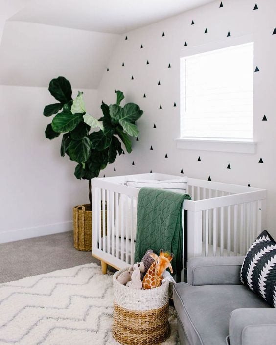 a contemporary nursery with a geo printed accent wall, a white crib, a grey chair, a potted plant, a color block basket