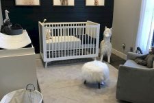a contrasting nursery with a black plank accent wall, a white crib and changing table, a grey chair, pretty toys and a print gallery wall
