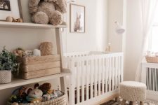 a cozy neutral nursery with a white crib, a crochet stool, a printed rug, an open shelving unit and some potted plants is cool