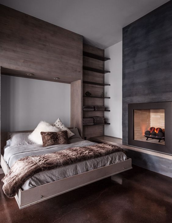 a cozy rustic bedroom with a taupe wooden accent wall, a fireplace clad with black wooden plants, a hidden bed and built-in shelves